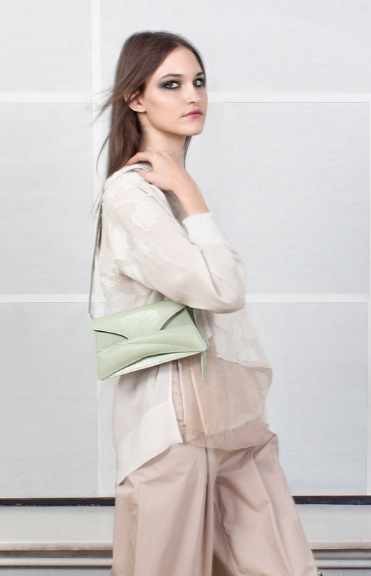 A person stylishly holding a light green Link Bag, shoulder bag with a quilted, sculpted, contemporary design and a soft wrist strap by Budapest based fashion design brand by Linda Sieto.