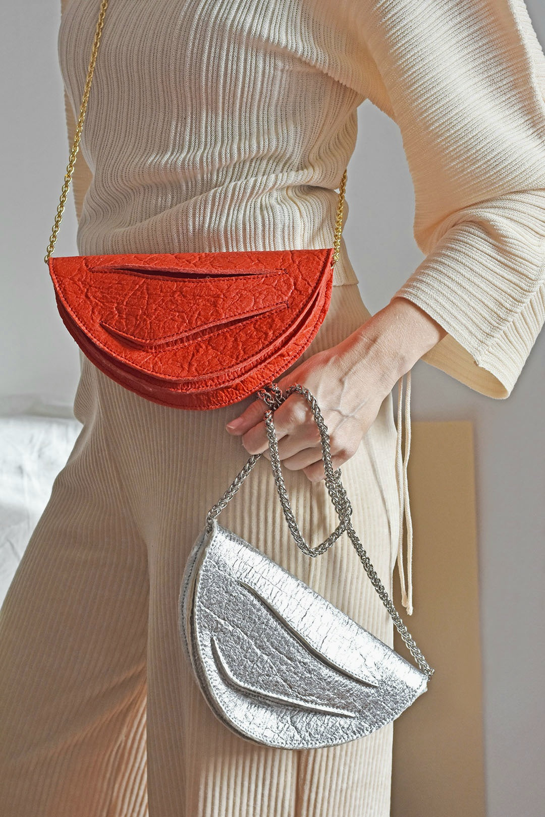 Person holding a red and silver crescent-shaped vegan designer handbag crafted in Budapest from pinatex