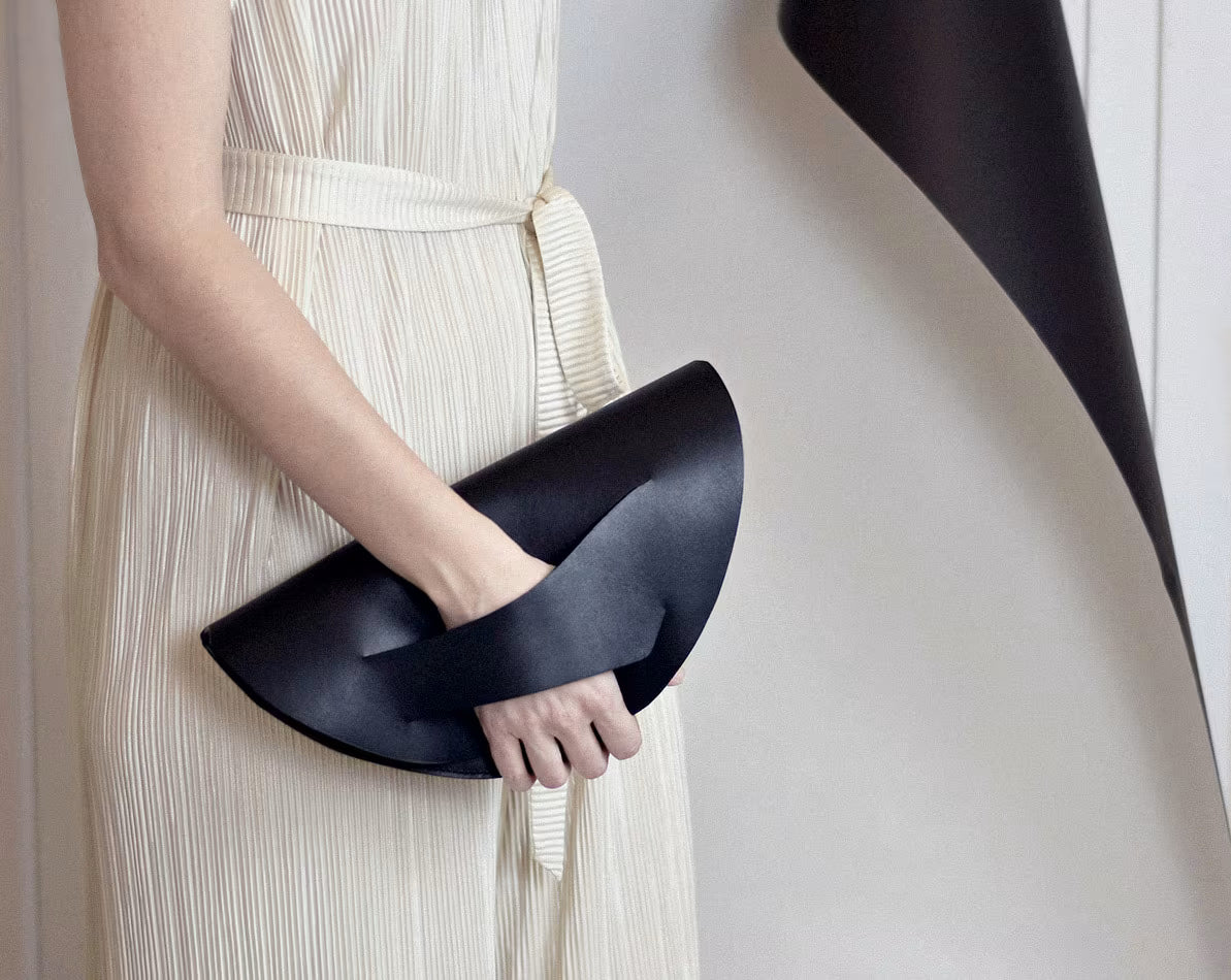 Fekete bőr magyar designer táska, válltáska, tervezői márka. Sculptural clutch bag, genuine Italian leather, quiet, alternative luxury, black  crescent handbag, crossbody purse with unique wrist strap by Hungarian, Budapest based brand. 