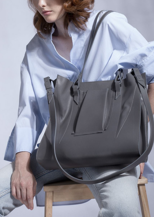 A steel grey colored tote bag with contrasting avantgarde, structured and soft design elements, made of Italian cow leather, with a pleated outer pocket, magnetic closure, and a detachable, adjustable shoulder strap.