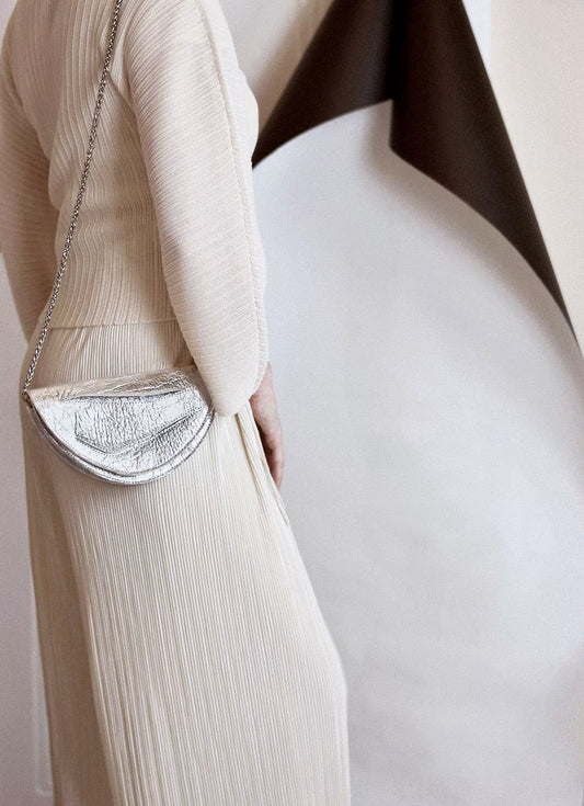 Sculptural clutch to shoulder bag handcrafted from plant-based,vegan material, elegant, silver handbag with unique wrist strap, by Budapest, EU based designer. Elegáns, magyar vegán designer borítéktáska, ezüst táska, magyar táska tervező márka.