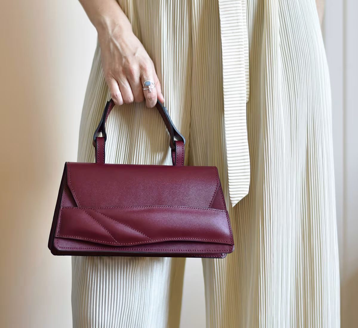 Handmade sculptural bag crafted from premium Italian nappa leather, black cherry red, oxblood coloured handbag, crossbody purse with unique wrist strap by Budapest based designer. Egyedi tervezésű, prémium, bordó valódi bőr alkalmi designer táska, kézzel festett élek, magyar tervezői márka.