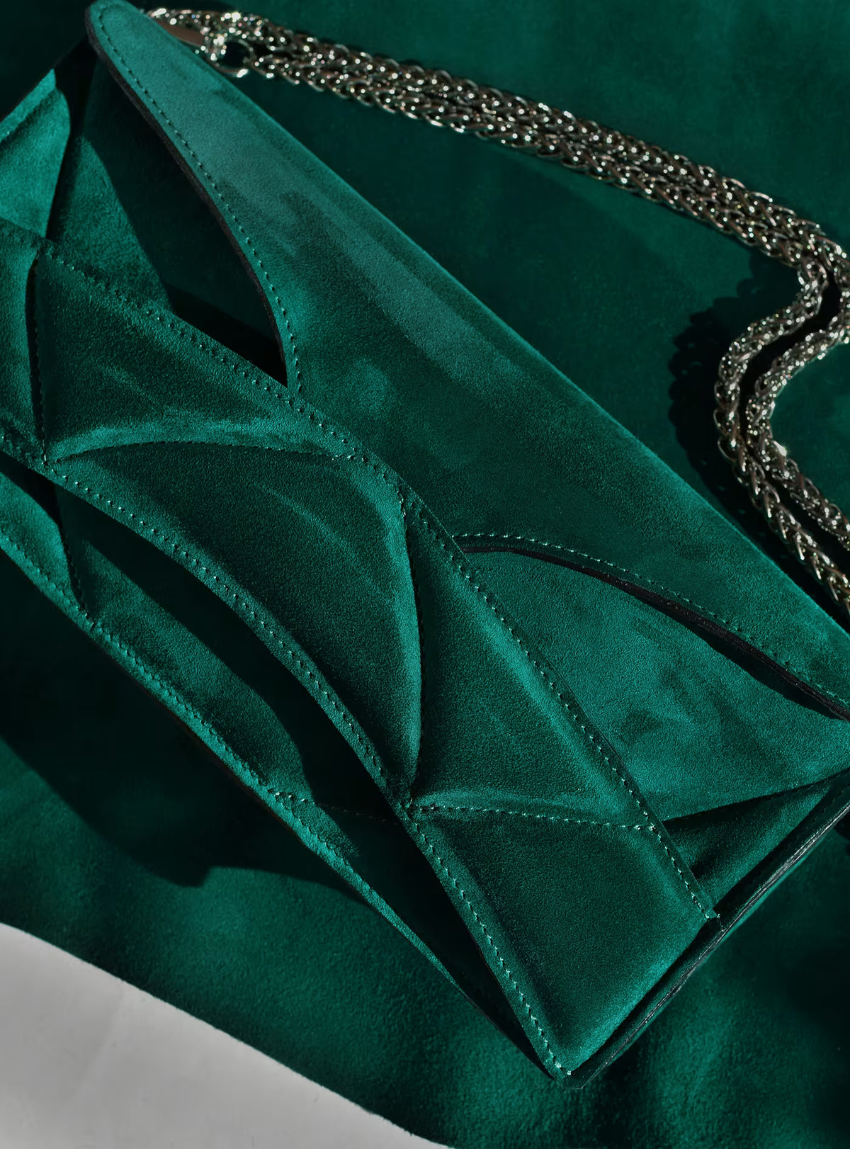 A close-up of Lindasieto's Abstract Heart Bag, in dark emerald green suede leather,  designer clutch bag with geometric stitched paneling and a silver chain shoulder strap.