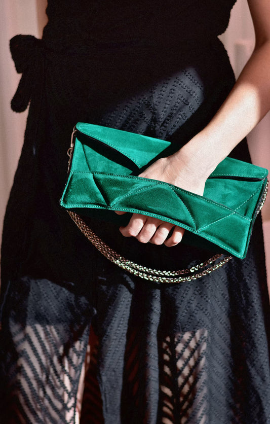 Person in black dress wearing LINDASIETO's Abstract Heart Bag in hand, in emerald green suede leather, designer clutch bag with layered heart pattern, sculptural wrist strap with a silver chain shoulder strap.