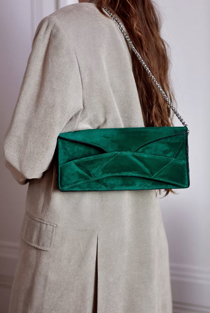Person in beige jacket wearing LINDASIETO's Abstract Heart Bag on the shoulder,  designer clutch bag with layered heart pattern, sculptural wrist strap with a silver chain shoulder strap. in emerald green suede leather.