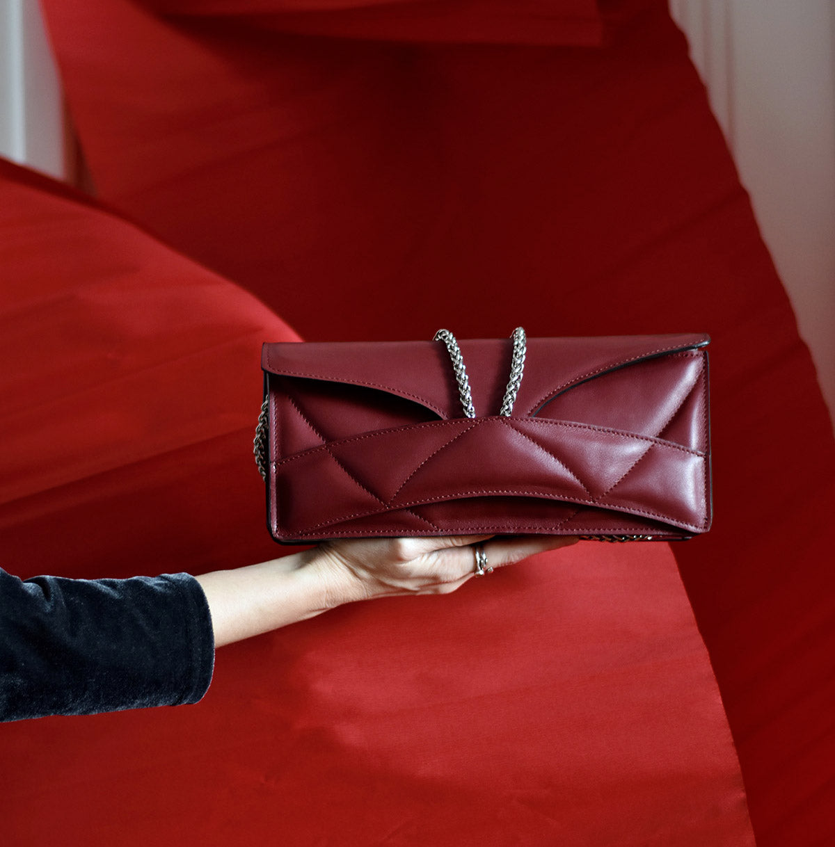 Prémium, elegáns, piros, bordó bőr designer táska, magyar tervezői táska márka, különleges színek, személyre szabott monogram. Dark red burgundy Italian leather, handcrafted sculptural occassion clutch bag, seen on Vogue, unique wrist strap, quiet, alternative luxury personalised gift, Budapest based fashion label.