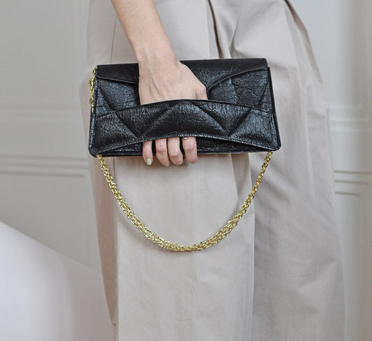 Handmade black Italian genuine leather, or vegan handbag, crossbody, oversize, soft clutch bag with unique wrist strap by Hungarian, Budapest based designer. Magyar designer vegán válltáska, clutch táska kézben tartva, arany lánccal, magyar táskatervező márka.