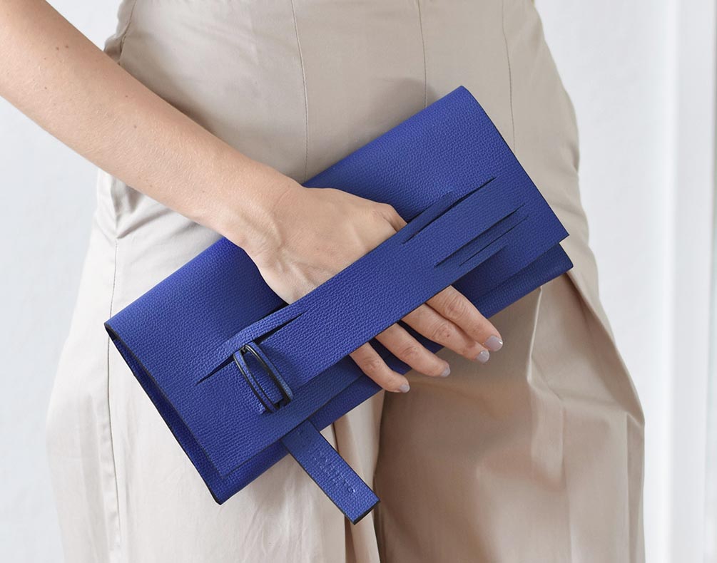 A person holding a lindasieto mini horizontal clutch in ultramarine blue leather with directional slashes.