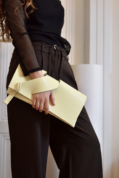 Lindasieto lemon cream, butter yellow leather Diagonal Slashed evening clutch purse, worn in hand with sculptural wrist strap, by Budapest based designer. Kortárs magyar designer vaj sárga bőr clutch táska,  különleges alkalmi outfit kézműves kiegészítő, művész tervező.