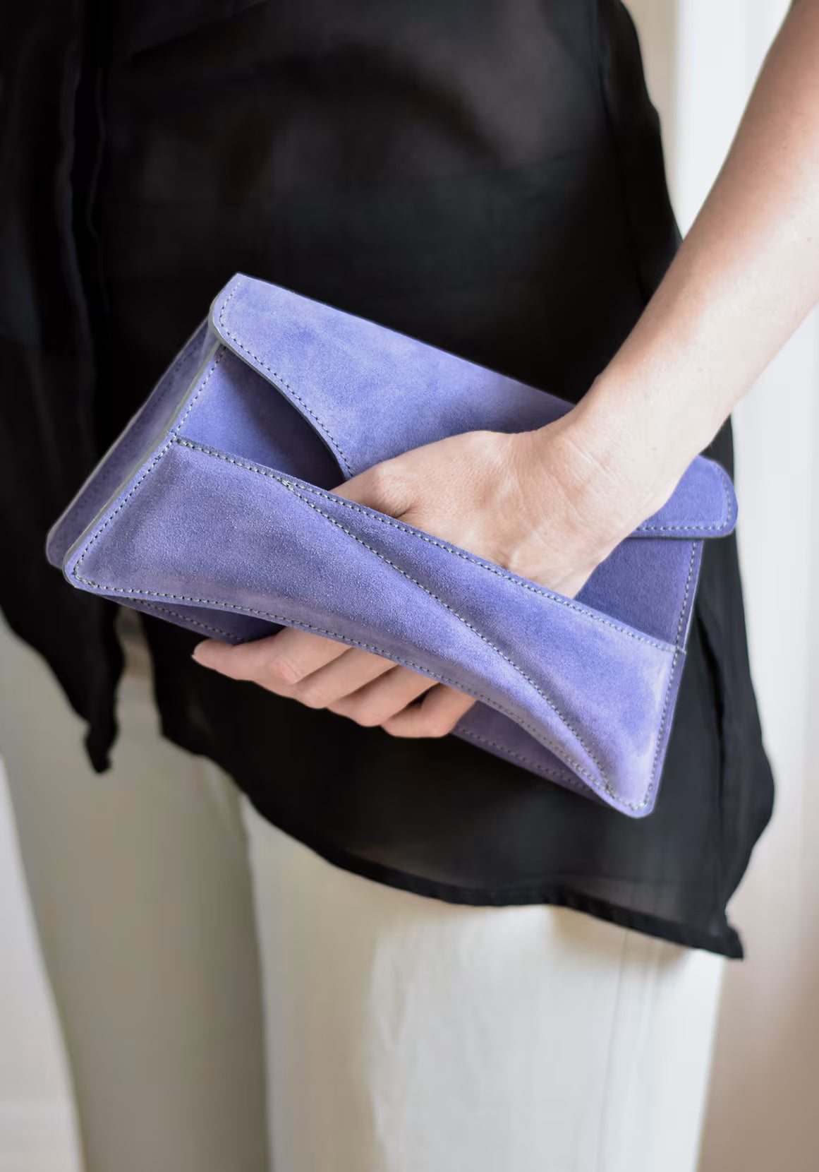 Lindasieto sculptural amethyst lilac suede leather Link Bag, designer handbag in hand with black elegant minimal outfit. Magyar kortárs designer lila velúr bőr alkalmi clutch táska, kézben viselve, elegáns fekete neutrális öltözékkel