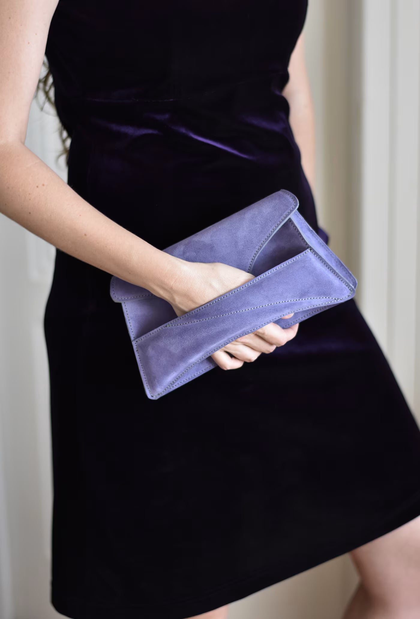 Lindasieto sculptural amethyst lilac suede leather Link Bag, designer occasion bag worn in hand with dark violet coloured elegant velvet outfit. Magyar kortárs designer lila velúr bőr alkalmi clutch táska, kézben viselve, elegáns padlizsán ruhával