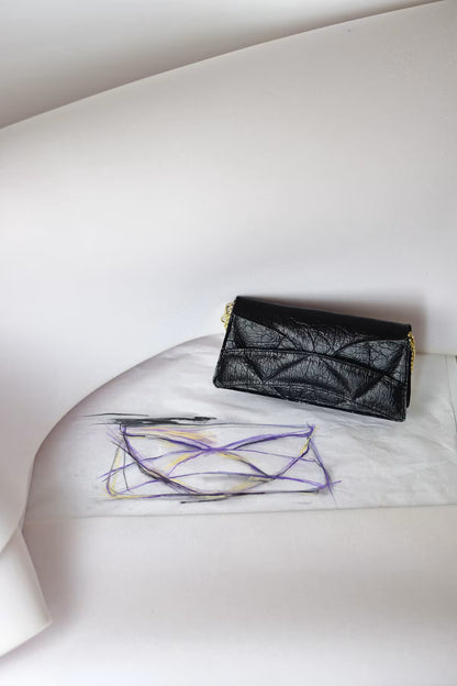 LINDASIETO Enigmatic Heart Bag from the Abstract Hearts collection in black vegan Pinatex. Sculptural clutch bag with gold-tone hardware sits on a white surface next to the original colorful abstract sketch by Linda Sieto on white paper, set against a minimalist white background.