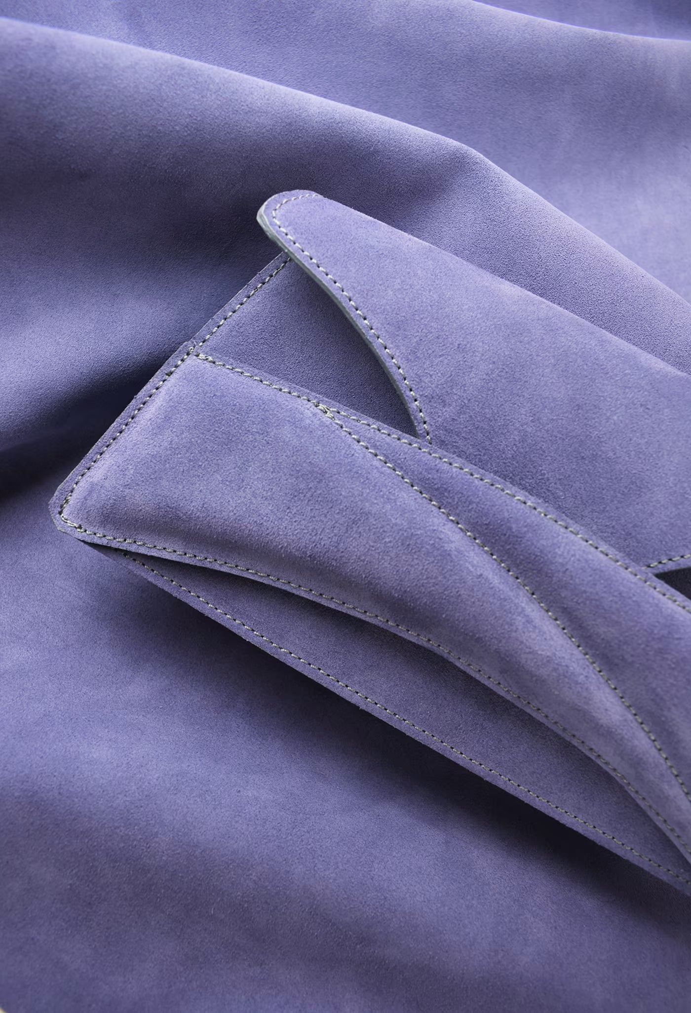 A close-up of a Lindasieto Link Bag, clutch in amethyst lilac purple suede leather with fine stitched edges and soft folds and leather texture. Magyar kortárs designer lila velúr bőr alkalmi női clutch táska, közeli részletfotó a puha olasz hasított bőrről és varrásvonalakról.