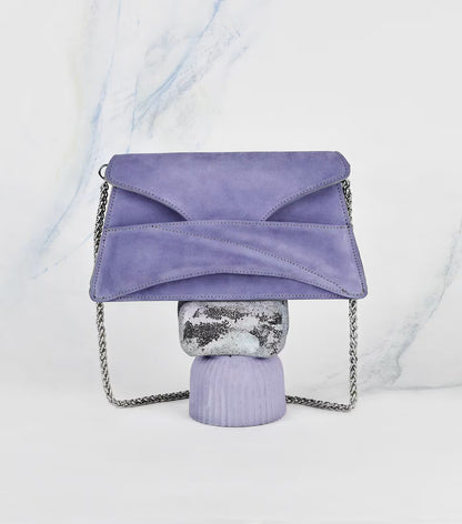 Lindasieto Link Bag, amethyst lilac purple envelope-style clutch with a chain strap, displayed on a decorative stand against a white marble-patterned background. Magyar kortárs designer lila velúr bőr alkalmi női clutch táska