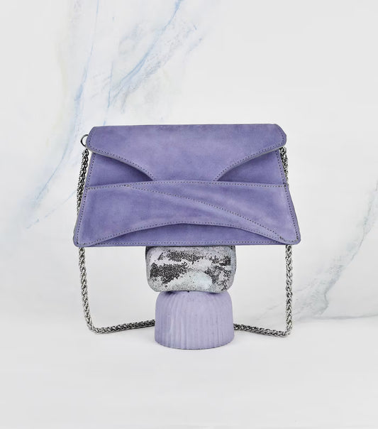 Lindasieto Link Bag, amethyst lilac purple envelope-style clutch with a chain strap, displayed on a decorative stand against a white marble-patterned background. Magyar kortárs designer lila velúr bőr alkalmi női clutch táska