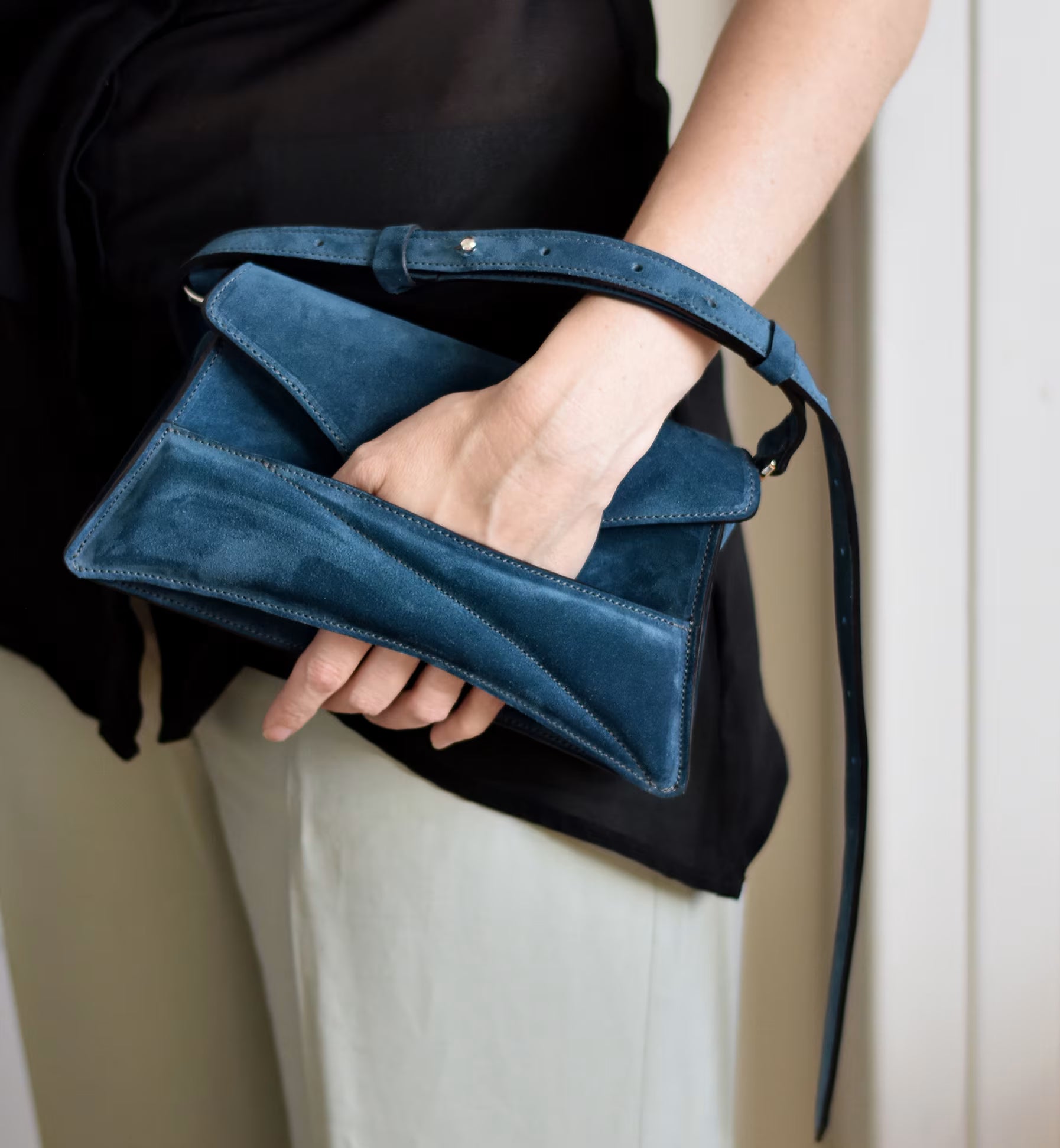 Lindasieto sculptural suede leather Link Bag in midnight azure blue, designer clutch to shoulder bag hybrid style worn in hand with unique, sculpted wrist strap with black and neutral minimal outfit. Magyar kortárs designer azúr kék velúr bőr alkalmi clutch, multiway táska.