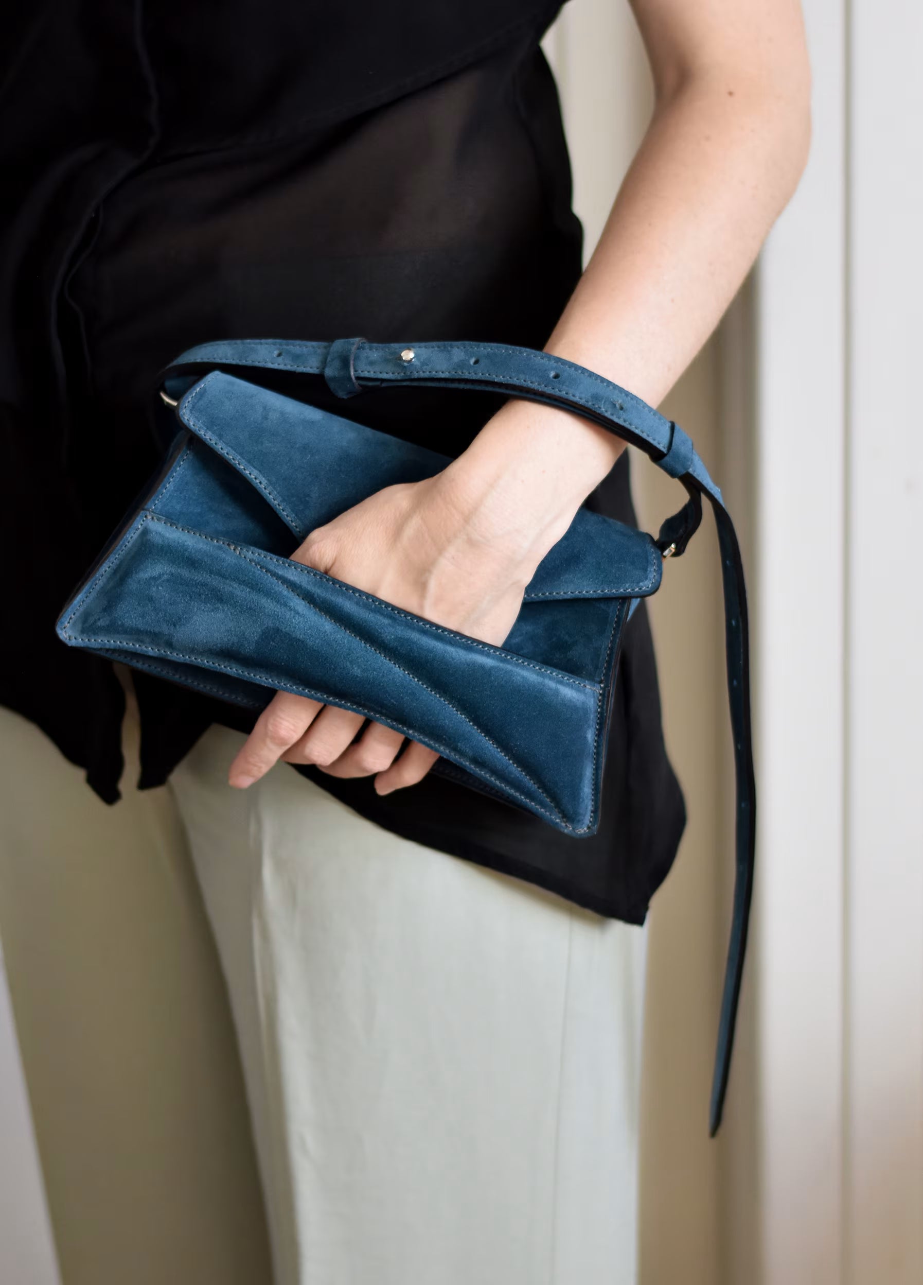Lindasieto sculptural suede leather Link Bag in midnight azure blue, designer clutch to shoulder bag hybrid style worn in hand with unique, sculpted wrist strap with black and neutral minimal outfit. Magyar kortárs designer kék velúr bőr alkalmi clutch multiway táska.