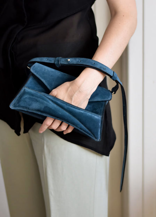 Lindasieto sculptural suede leather Link Bag in midnight azure blue, designer clutch to shoulder bag hybrid style worn in hand with unique, sculpted wrist strap with black and neutral minimal outfit. Magyar kortárs designer kék velúr bőr alkalmi clutch multiway táska.