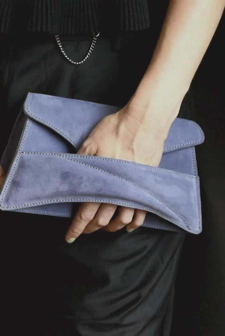Lindasieto sculptural amethyst lilac suede leather Link Bag, designer crossbody handbag worn on the shoulder with black elegant minimal outfit. Magyar kortárs designer lila velúr bőr alkalmi clutch táska, kézben viselve, elegáns fekete neutrális öltözékkel