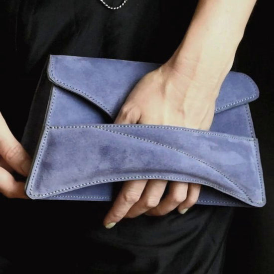 Lindasieto sculptural amethyst lilac suede leather Link Bag, designer crossbody handbag worn on the shoulder with black elegant minimal outfit. Magyar kortárs designer lila velúr bőr alkalmi clutch táska, kézben viselve, elegáns fekete neutrális öltözékkel