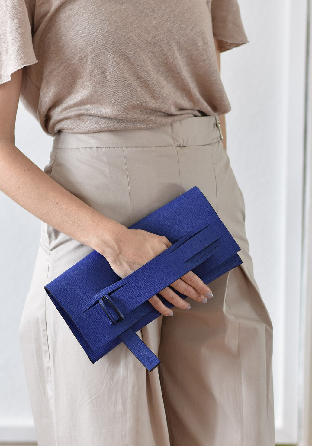 A person holding a lindasieto mini horizontal clutch in ultramarine blue leather with directional slashes.