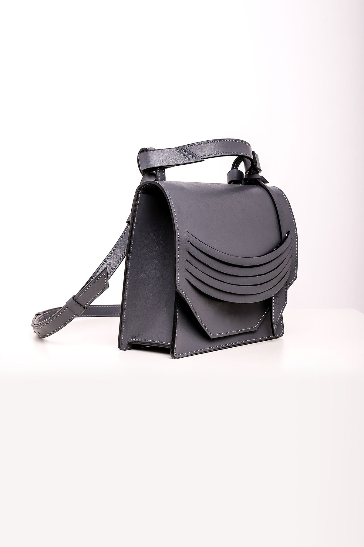 A steel grey leather shoulder bag with a structured design, featuring a top handle and adjustable shoulder strap. The bag is displayed against a white background.