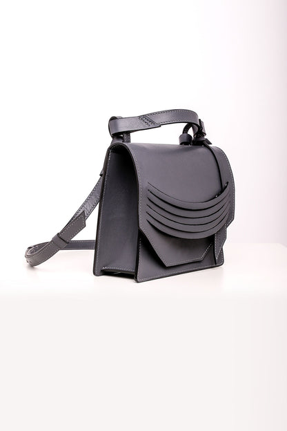A steel grey leather shoulder bag with a structured design, featuring a top handle and adjustable shoulder strap. The bag is displayed against a white background.
