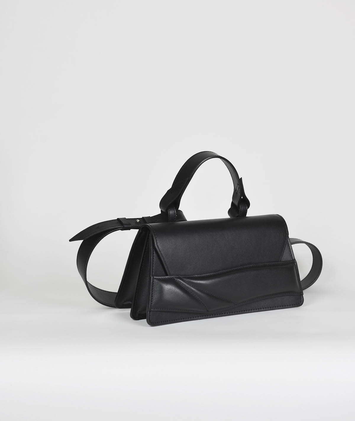Black leather contemporary two compartment handbag with sculptural, matelasse wrist strap design. Fekete bőr designer crossbody táska egyedi pánt, kézifogóval, vállpánttal.