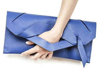 Royal blue contemporary leather clutch bag, pochette with unique wrist strap, worn in hand.  Egyedi bőr boríték táska, csukló pánttal, kék színben, magyar márka terméke.