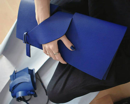 Blue contemporary genuine leather clutch bag, purse with unique wrist strap handle, worn in hand. Egyedi bőr boríték táska, csukló pánttal, kék színben, magyar márka terméke.