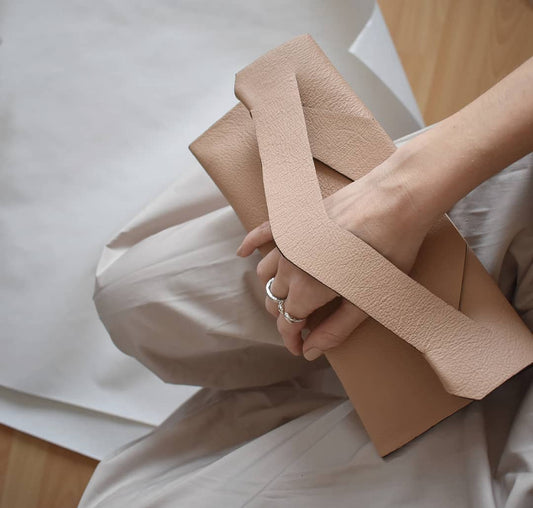 Beige, caramel contemporary genuine leather clutch bag, bridal purse with unique wrist strap, worn in hand. Egyedi bőr boríték táska, csukló pánttal, nude beige színben, magyar márka terméke.